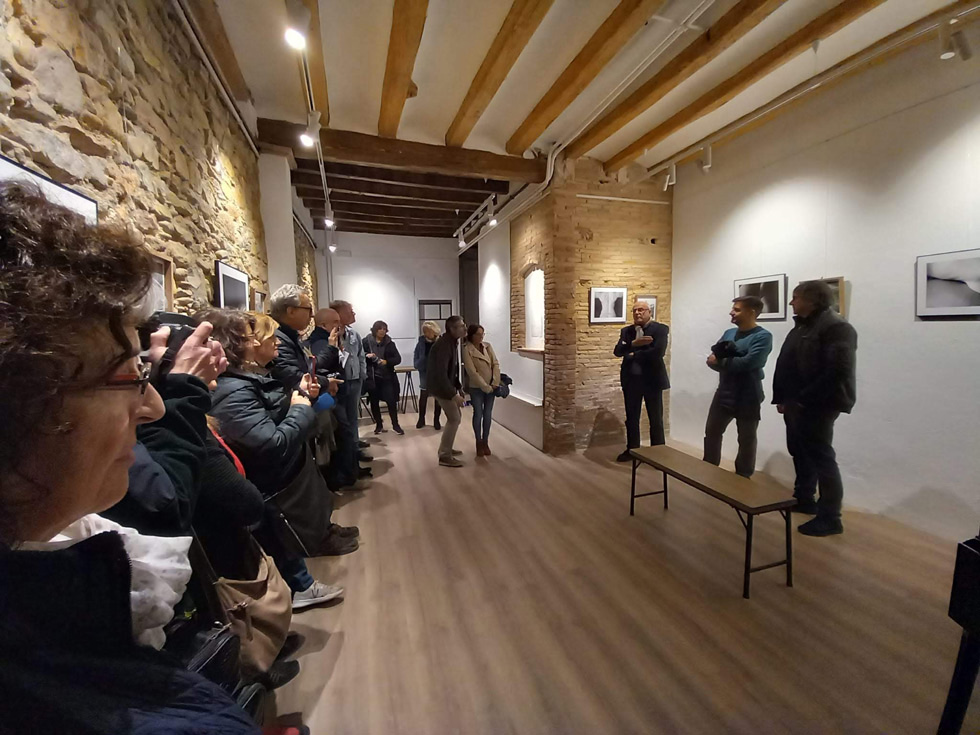 Visitors gathered in a photography gallery with rustic stone walls, listening to a presentation about the exhibited artwork.