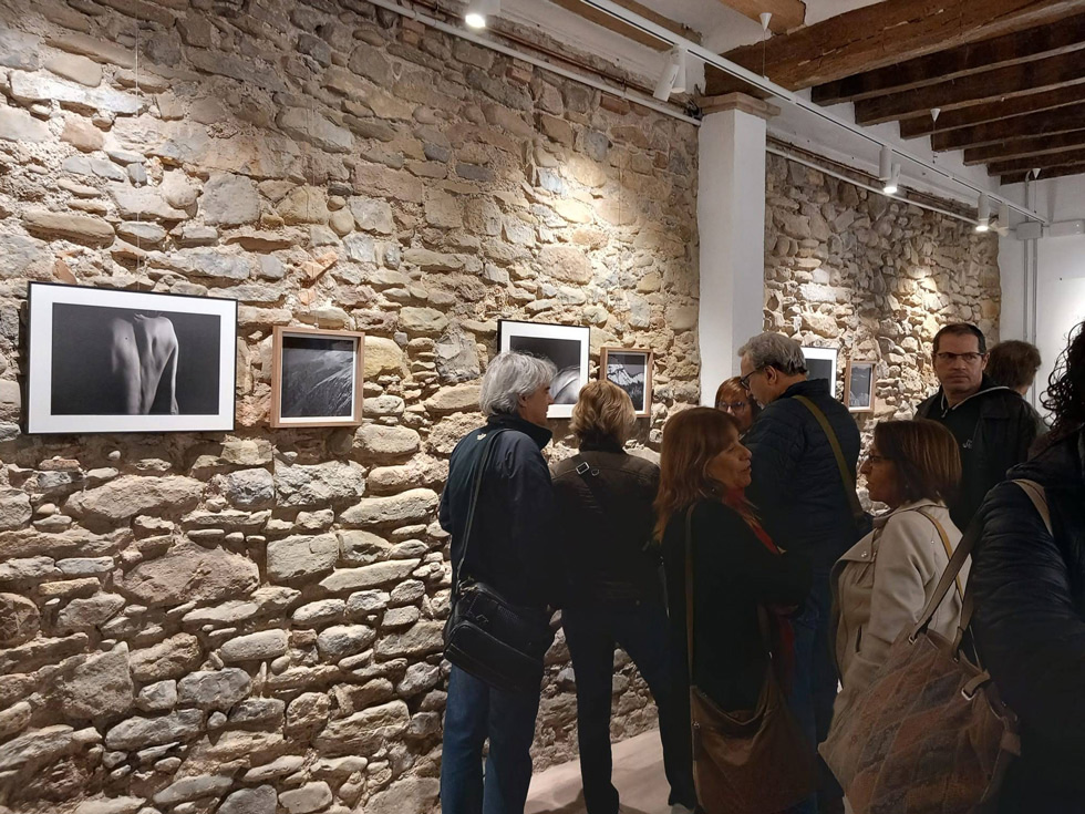 Gallery visitors examining black-and-white photographs displayed on rustic stone walls, during the crowded opening day.