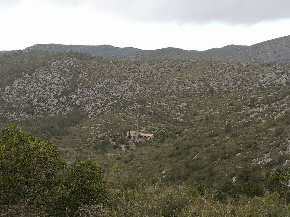 A secluded house nestled in a rugged, mountainous landscape with sparse vegetation.