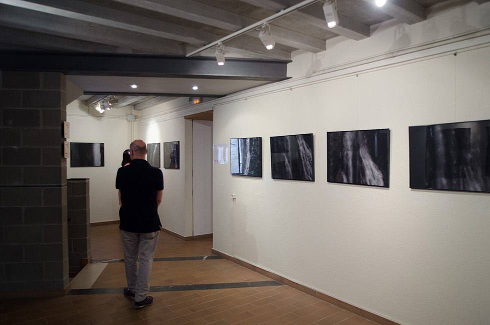 Visitor viewing framed photographs in a gallery with a tiled floor and exposed ceiling beams.