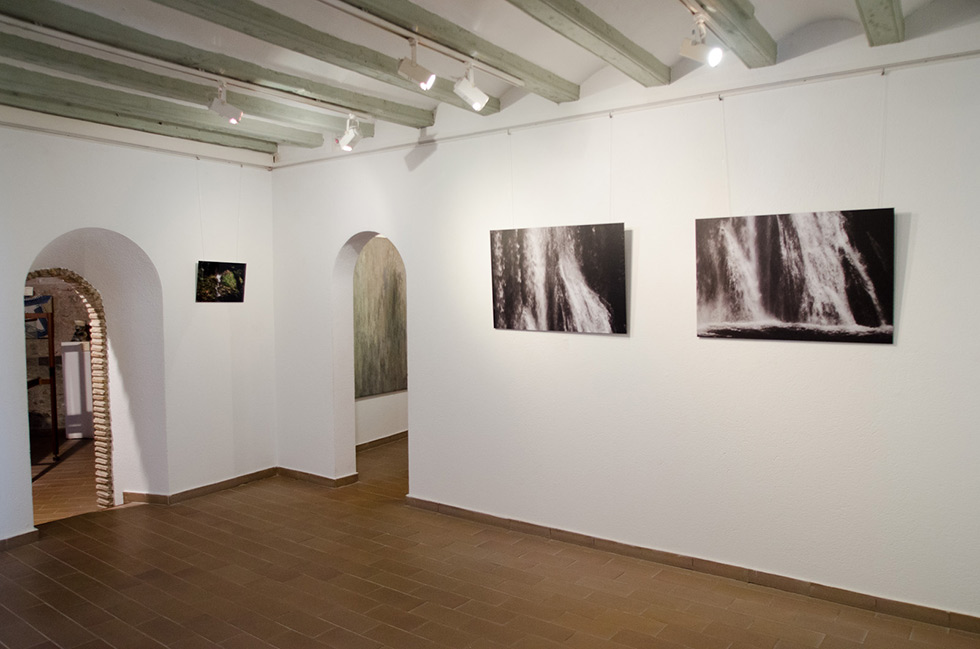 Gallery with wooden ceiling beams, tiled floor, and waterfall photographs on white walls.