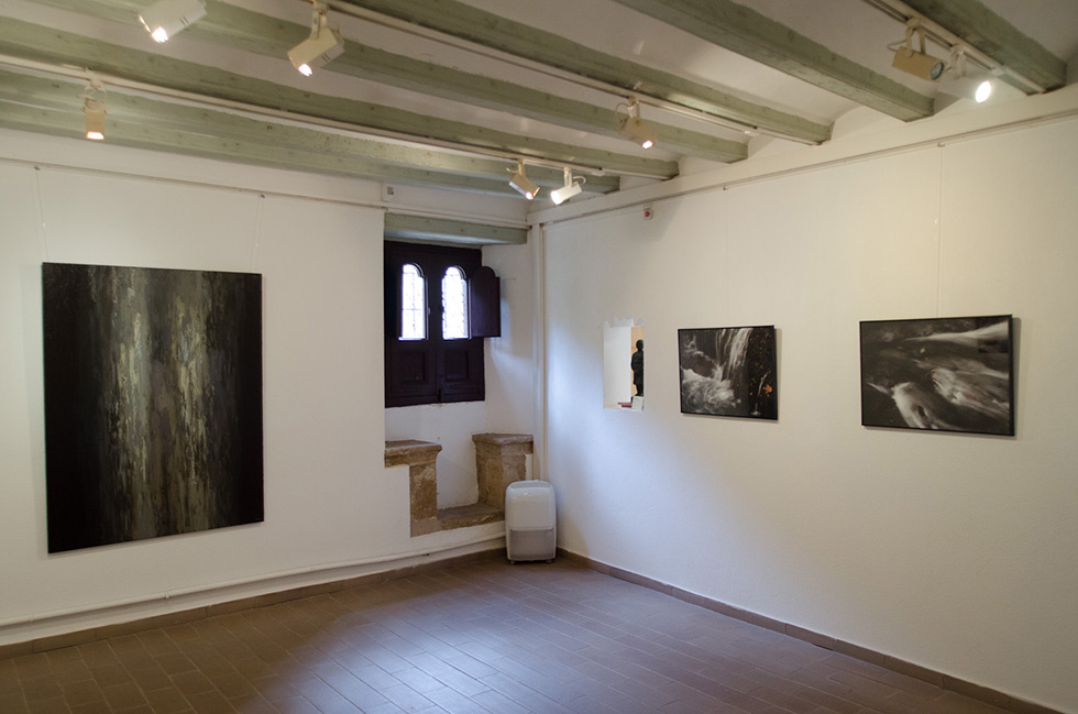 Room with wooden ceiling beams, tiled floor, waterfall photographs on white walls, and a small gothic window with wooden shutters and medieval stone window seat.