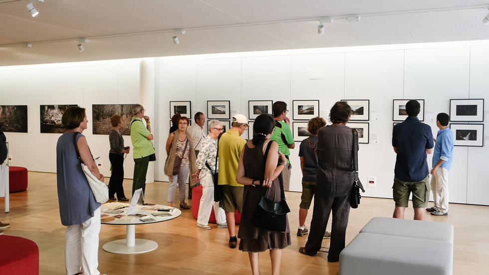 People browsing framed photographs in a spacious, well-lit art gallery.