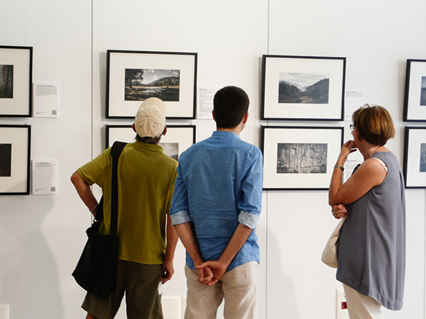 Three people closely examining framed landscape photographs on a gallery wall.