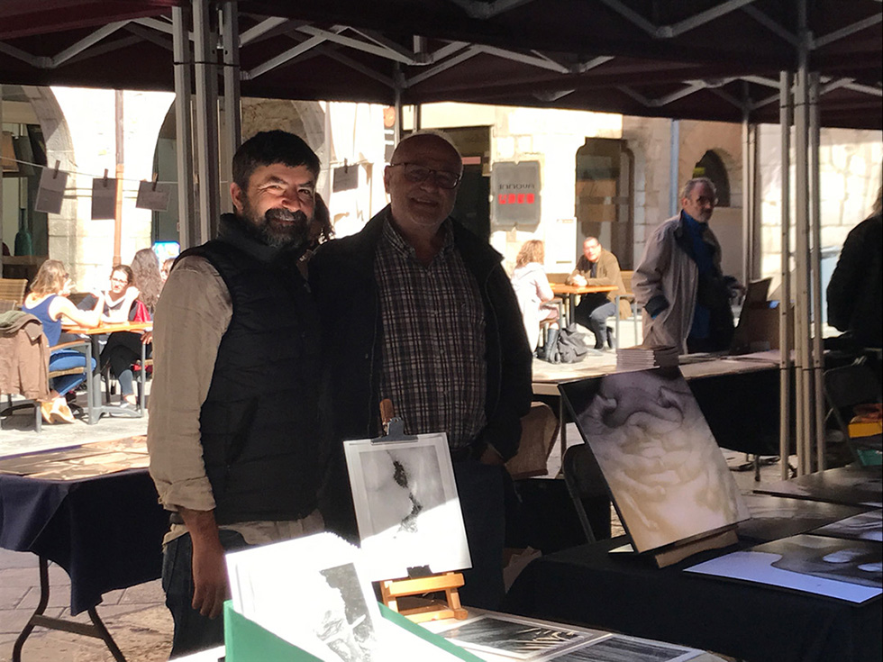 Two men standing next to a display of artworks at an outdoor photography fair.