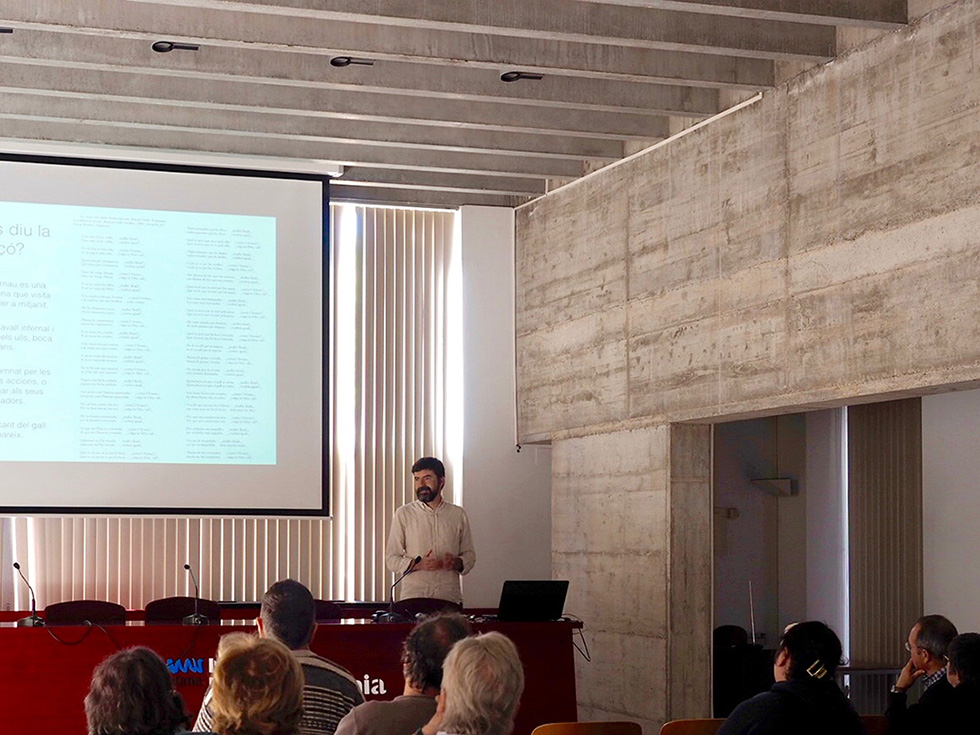 Man giving a presentation in a conference room with a projected screen and seated audience.