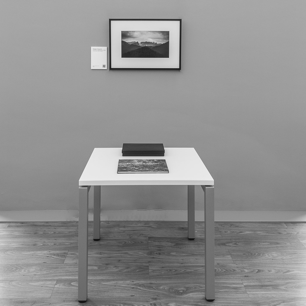 A single framed photograph on a grey wall above a white table displaying a book and a box.