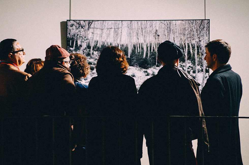 People gathered closely, viewing a large landscape photograph in an exhibition.