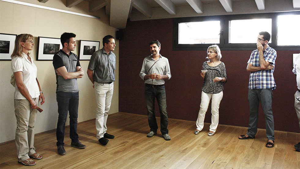 Group of people standing in an art gallery, listening to a man speaking.