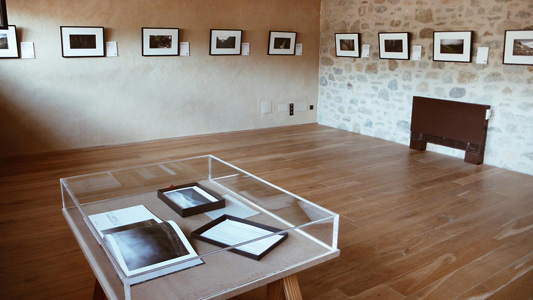 Gallery with framed photos on stone walls and a display table in the center with photographs and documents.