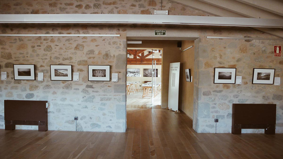 Room with framed photos on stone walls and an open doorway leading to another room with more framed photos.