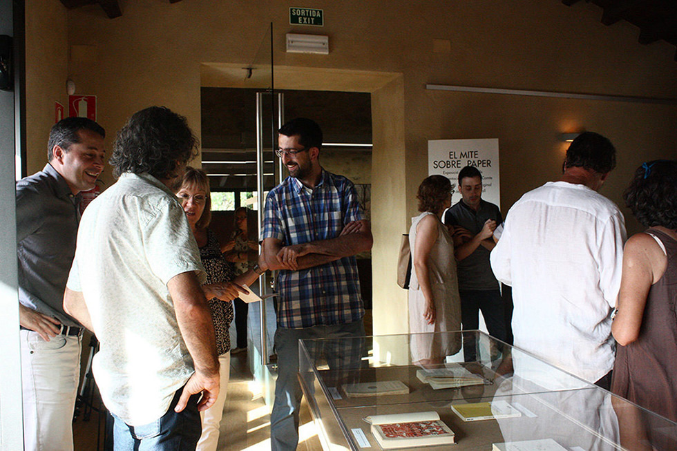 People conversing around a display case with books and papers.