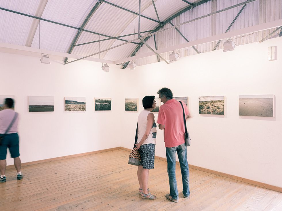 Two people talking in a gallery room with landscape photographs on the wall.