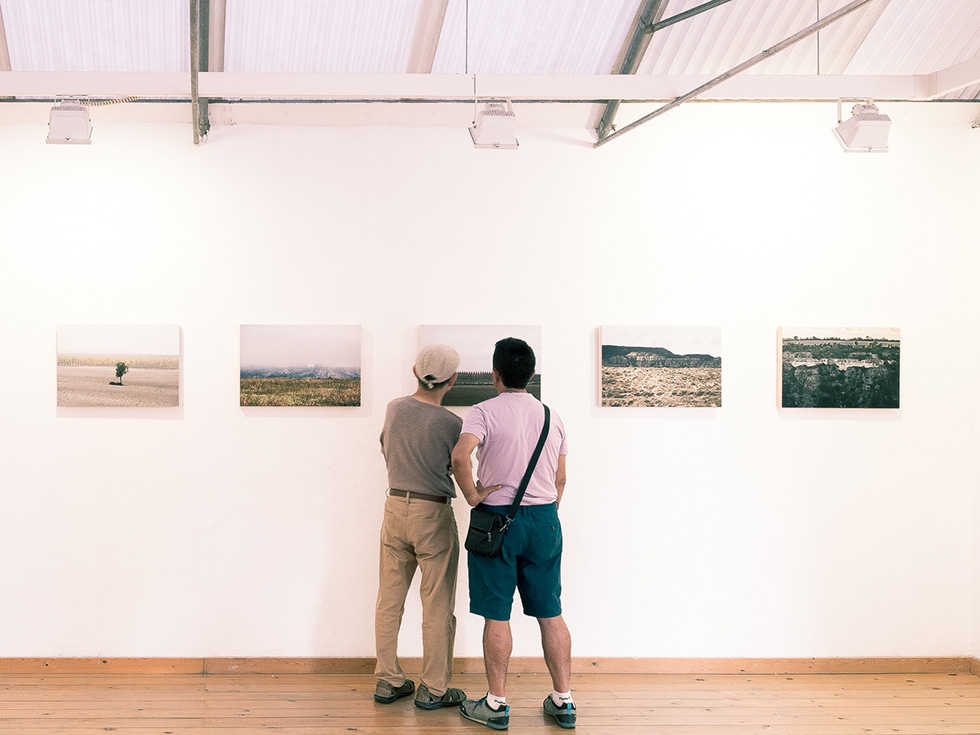 Two people closely viewing a photograph in a gallery room with landscape photographs on the wall.