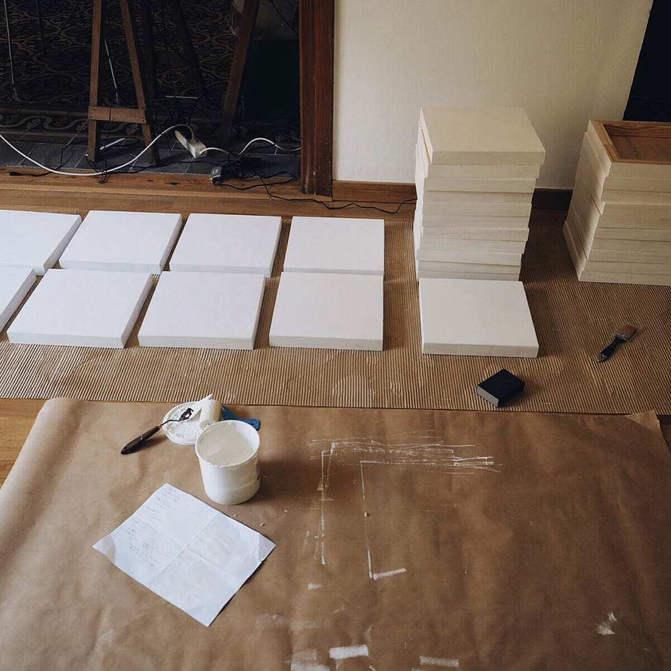 Art supplies, blank canvases, and stacks of frames laid out on the floor, ready for preparation in an artist's workspace.