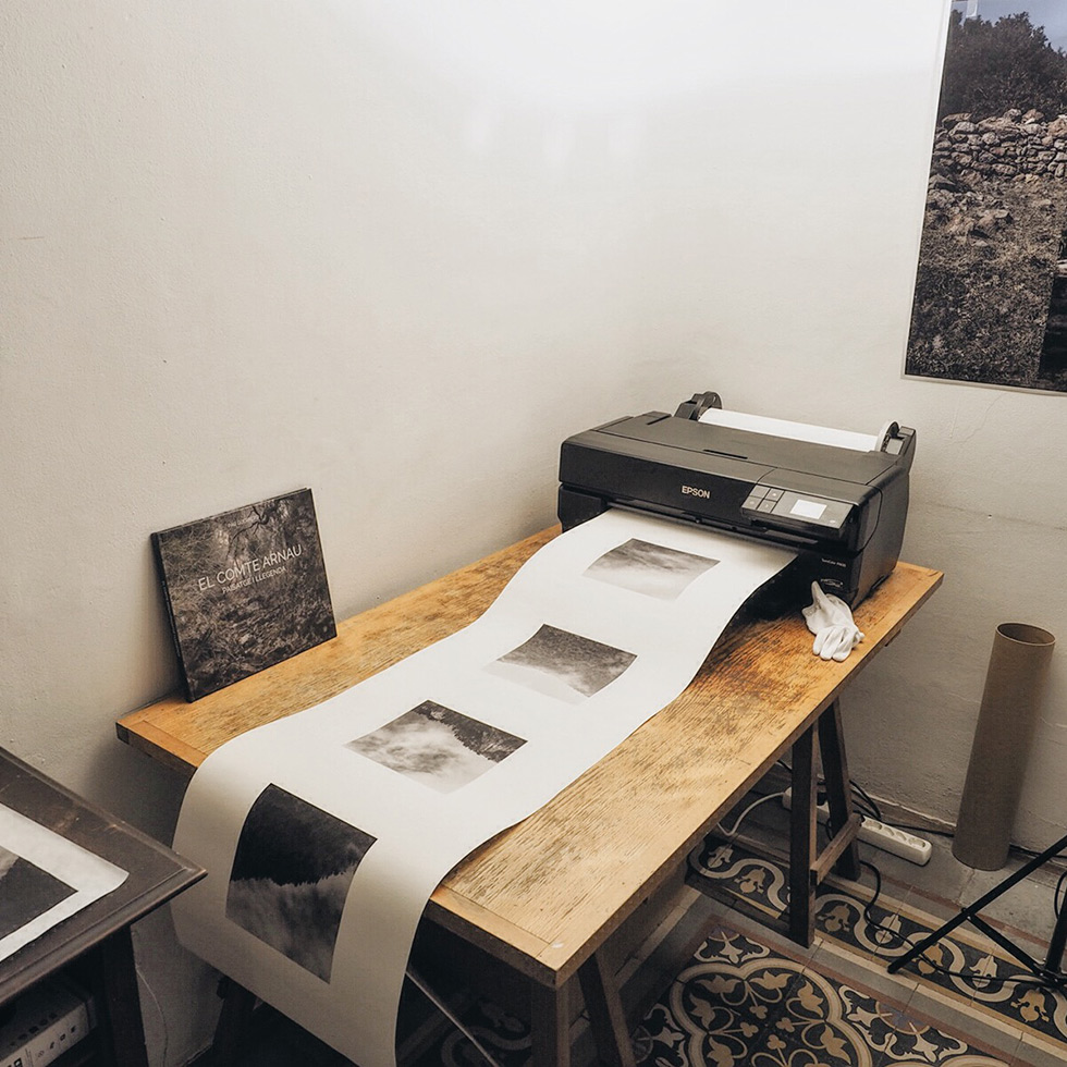 A printer on a wooden table producing a long strip of black and white photographs.