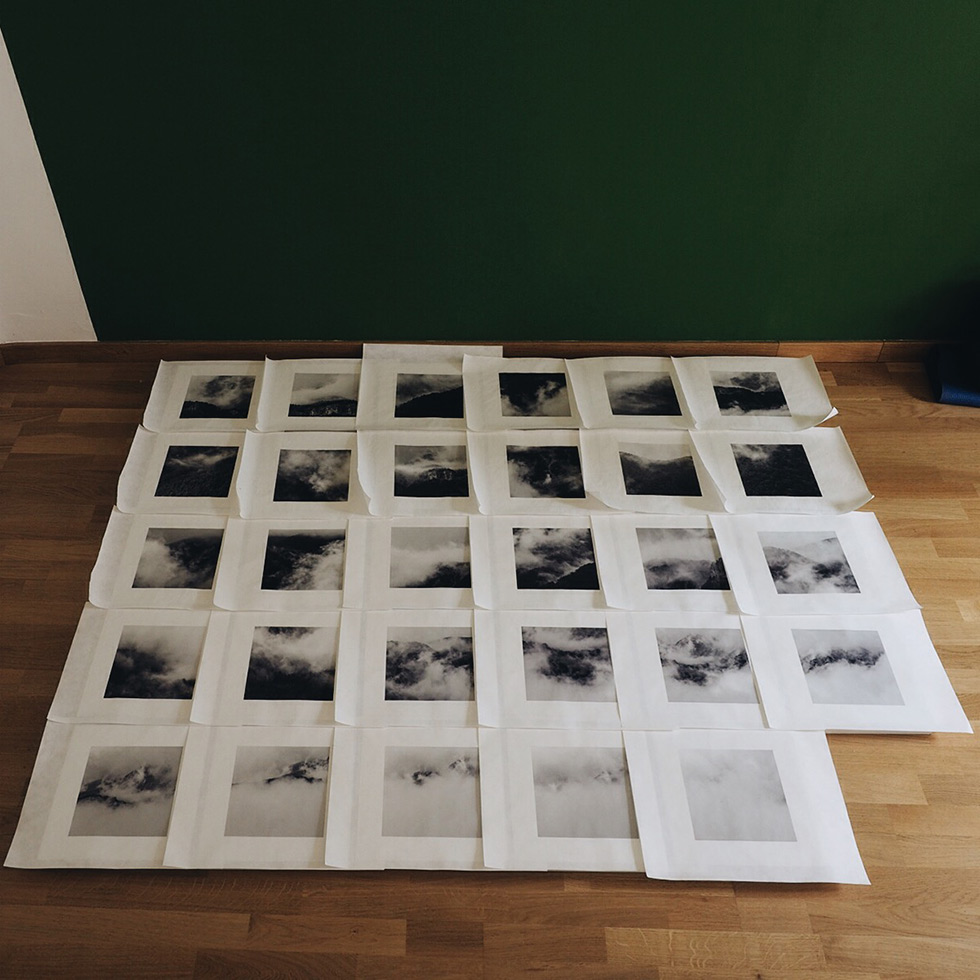 A grid of black and white photographs laid out on a wooden floor.