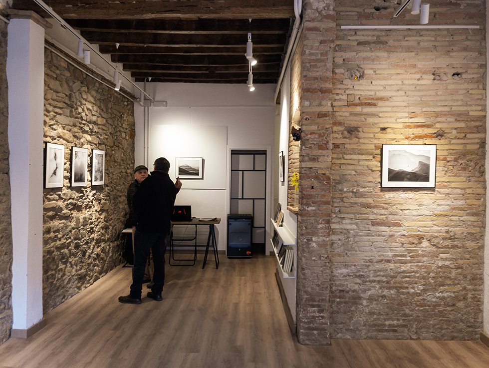 Two people discussing at a photography exhibition featuring black and white landscape photos on stone and brick walls.