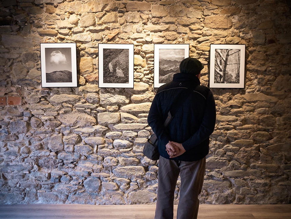 A man observing black and white landscape photographs displayed on a stone wall in an art gallery.