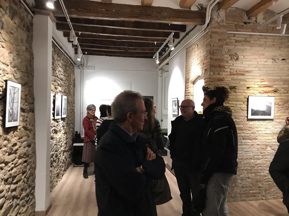 People viewing black and white landscape photographs on stone walls at an art gallery opening.