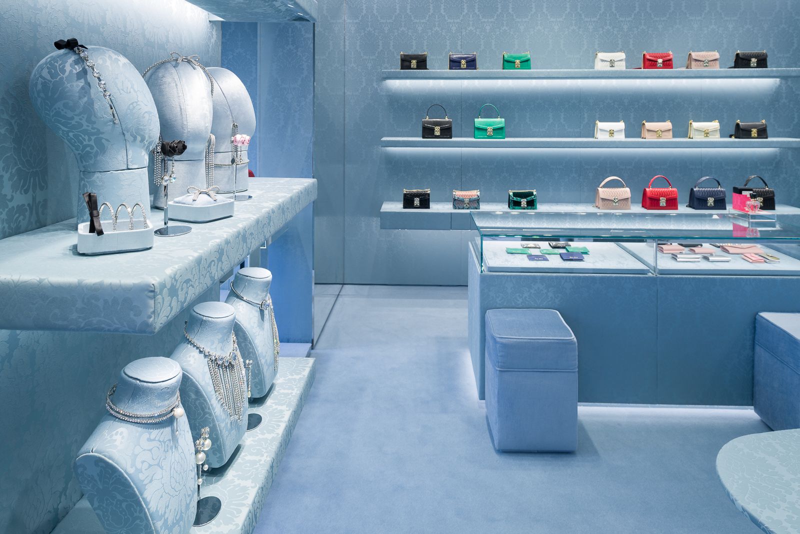 Joyería y bolsos exhibidos en una tienda Miu Miu con paredes y estantes texturizados azules.