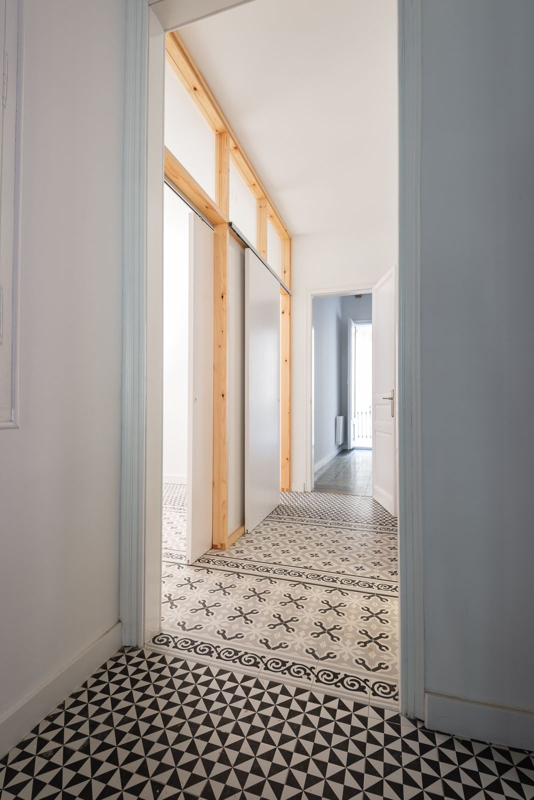 Pasillo con baldosas de suelo estampadas y elementos de marco de madera que conducen a una habitación luminosa.