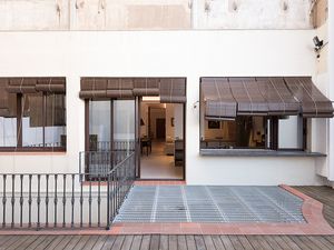 Patio al aire libre con barandilla metálica, terraza de madera y grandes ventanas con persianas de bambú, que conduce a un interior moderno.