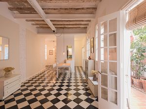 Espaciosa área de comedor con baldosas de suelo de tablero de ajedrez, vigas expuestas y puertas francesas que se abren a un área de patio.