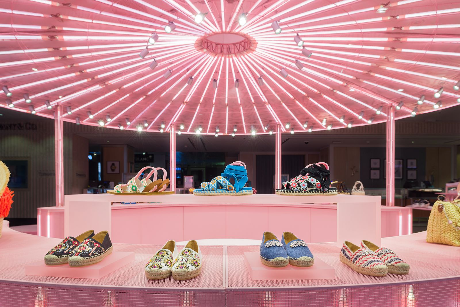 Sandalias y alpargatas de colores brillantes exhibidas bajo un dosel rosa radiante en la vibrante tienda pop-up de Miu Miu.