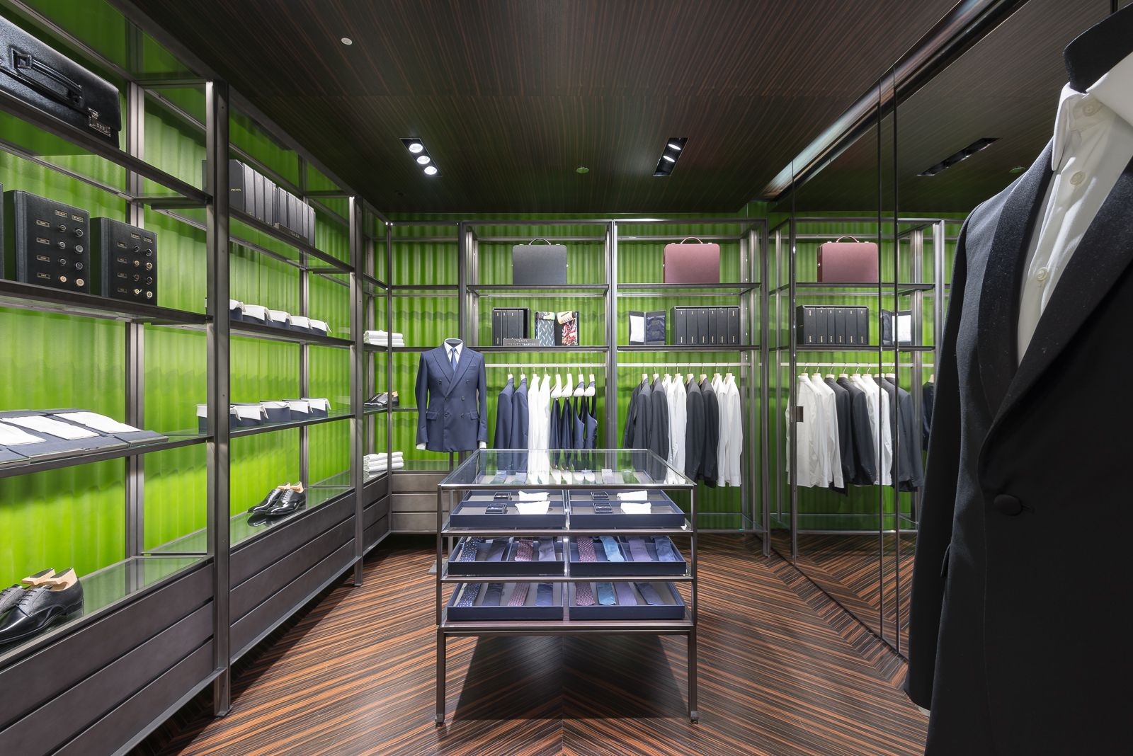 Interior de tienda de lujo con estantes que muestran trajes de hombre, camisas de vestir, corbatas y zapatos formales.