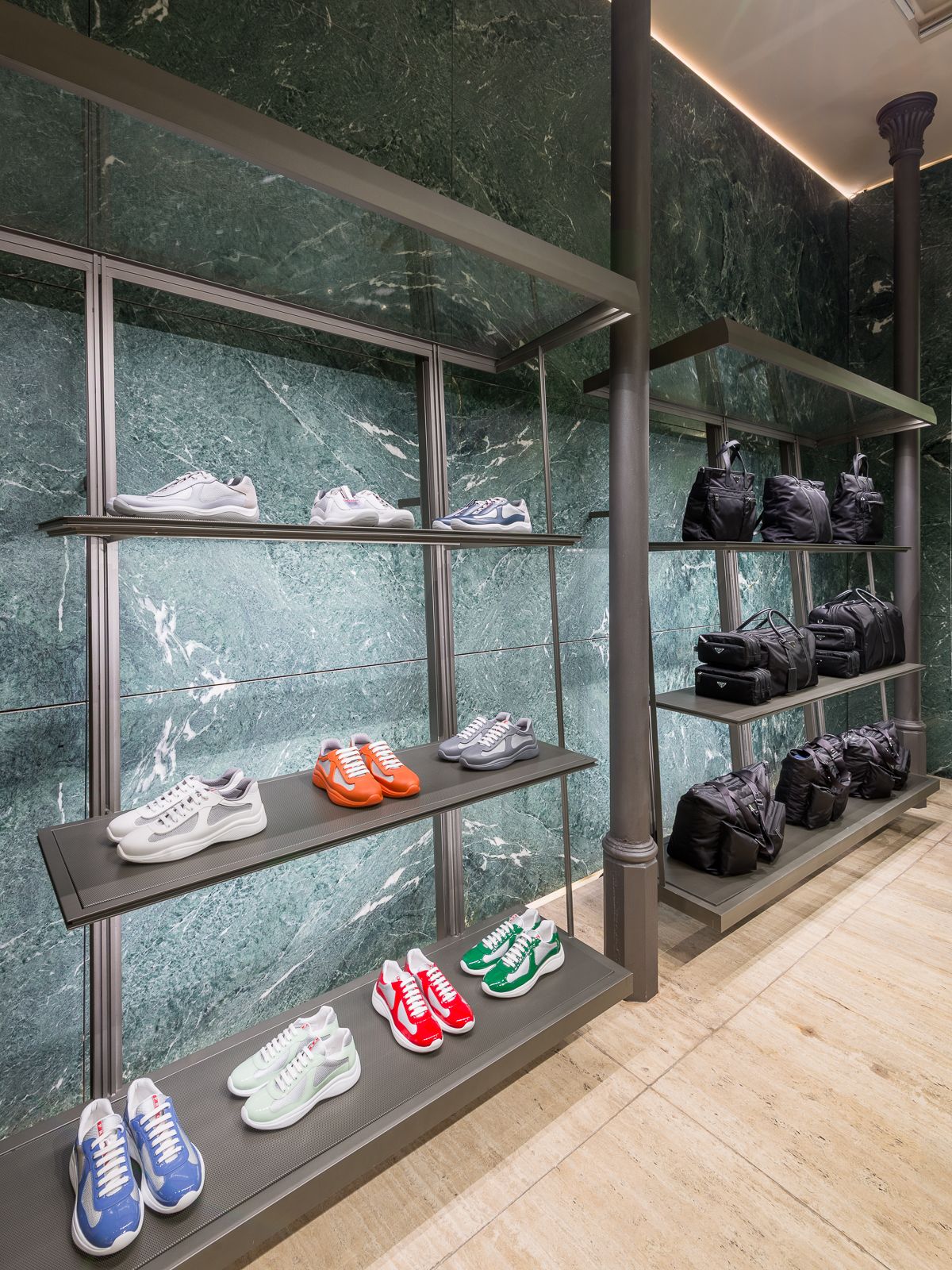 Lujosa boutique Prada con paredes de mármol verde, mostrando zapatillas de diseño y bolsos negros en elegantes estanterías metálicas.