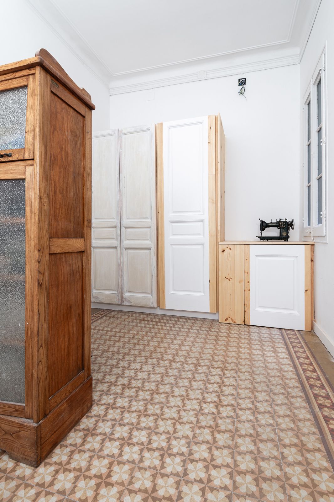 Habitación con muebles vintage, baldosas de suelo estampadas y una máquina de coser sobre un armario de madera.