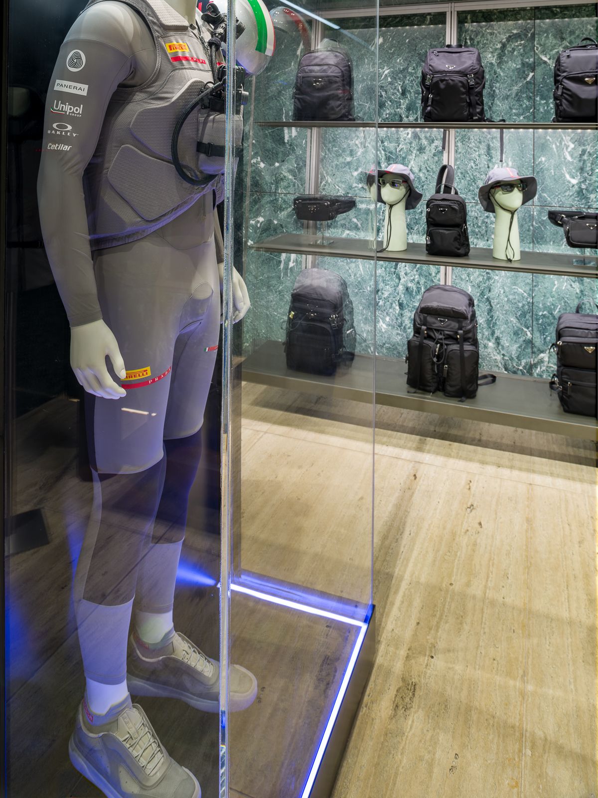 Lujosa boutique Prada con paredes de mármol verde, mostrando un maniquí en un atuendo de rendimiento encerrado en una vitrina de vidrio.