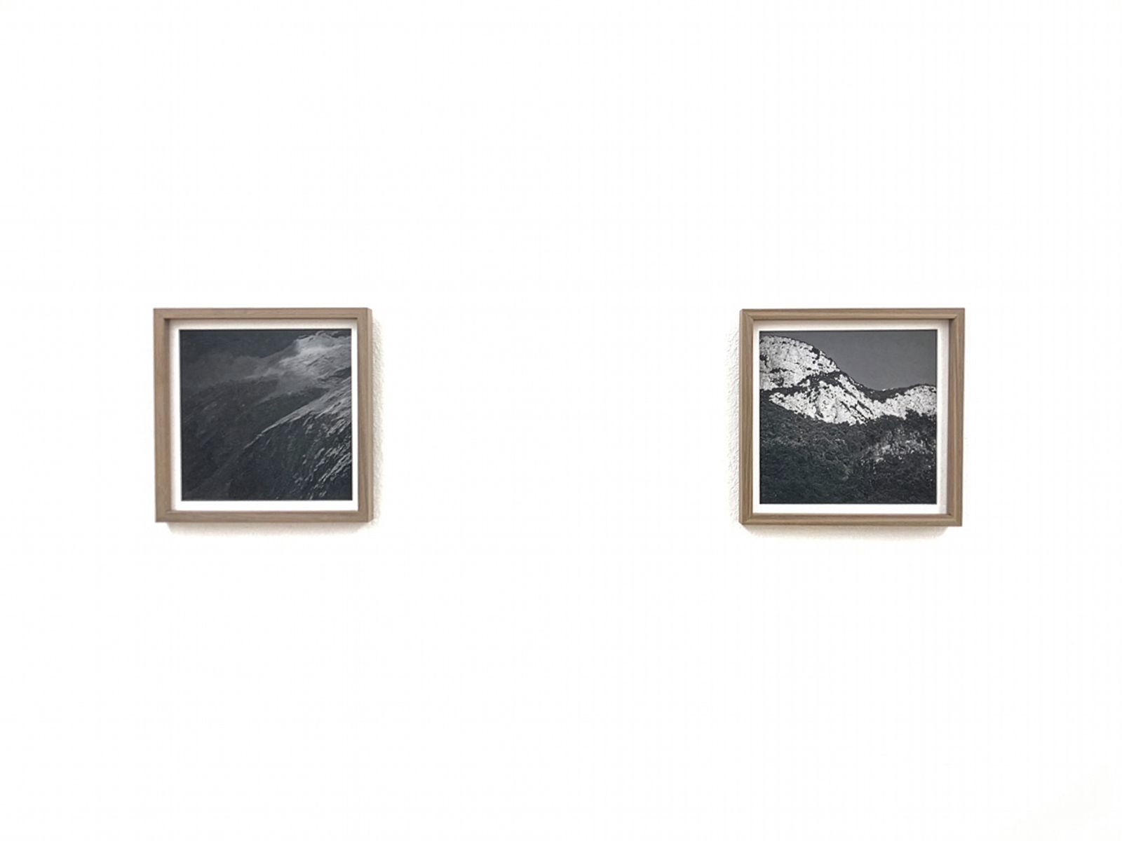 Dues fotografies emmarcades en blanc i negre de muntanyes exposades en una paret blanca en un entorn de galeria minimalista.