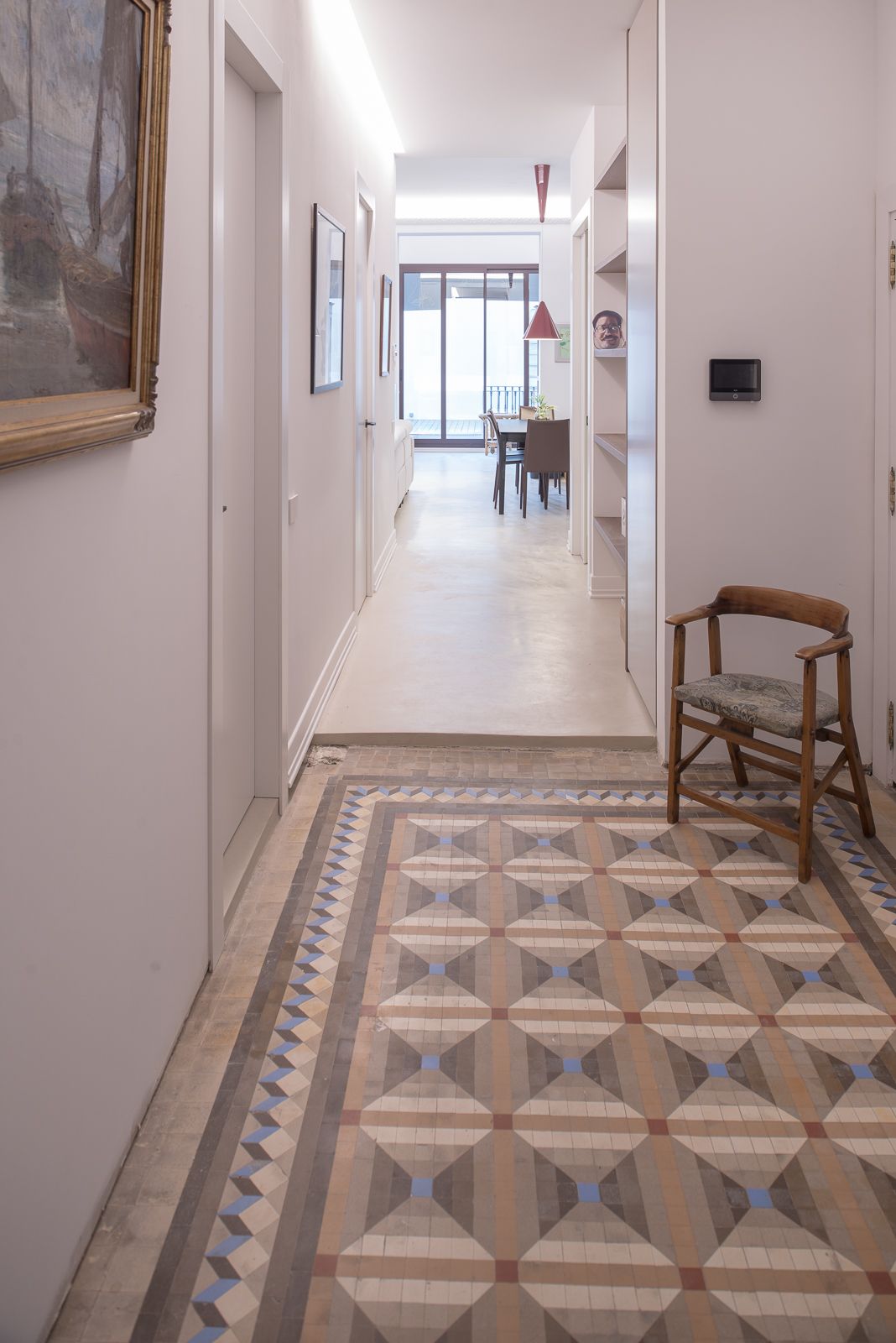 Hallway with geometric tiled floor, leading to a dining area with a red pendant lamp.