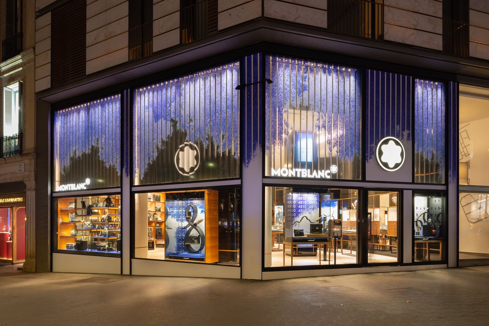 Exterior de tienda Montblanc por la noche con ventanas iluminadas mostrando productos y diseño artístico azul.