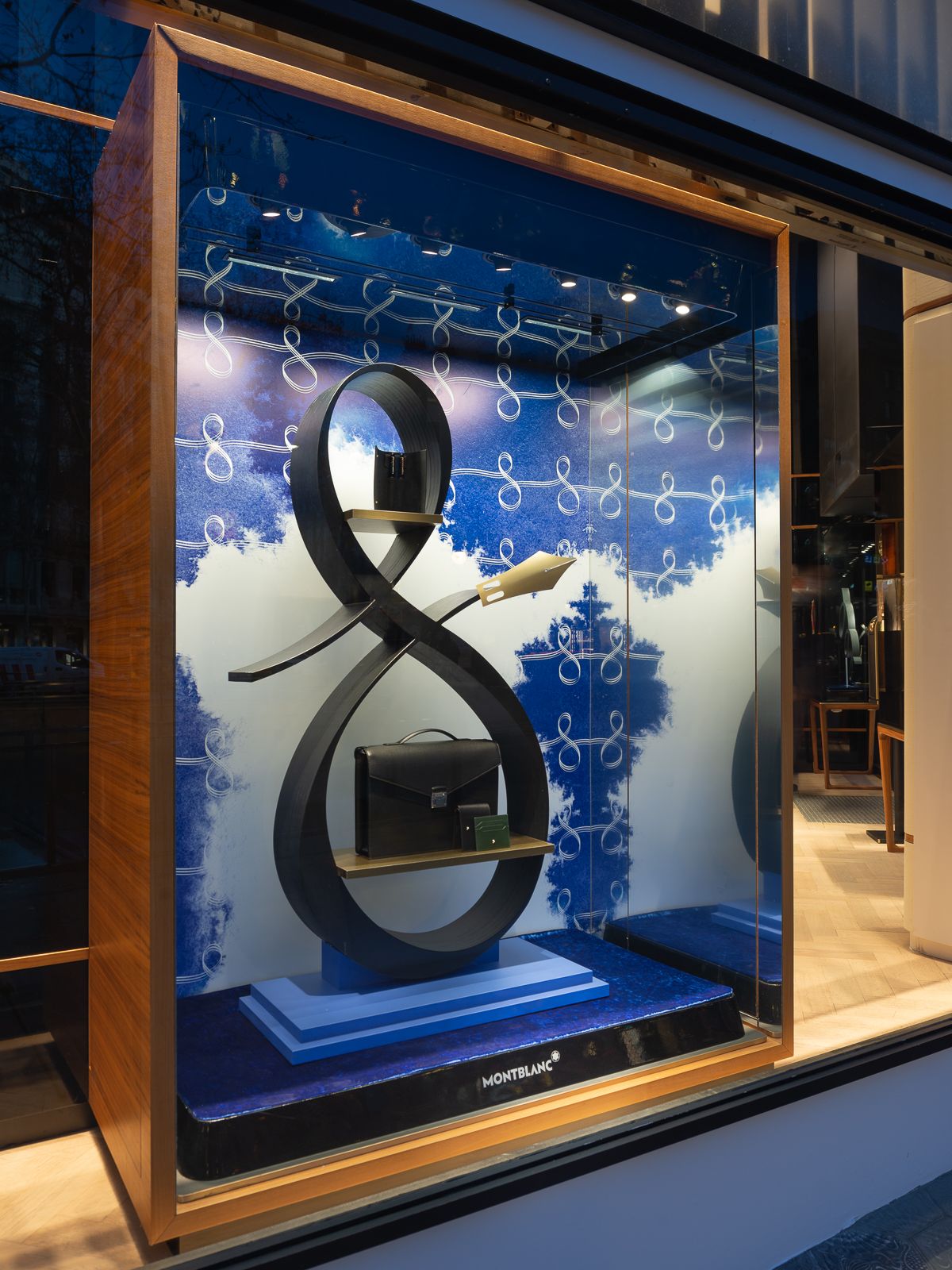 Escaparate de tienda Montblanc con un gran símbolo de infinito negro con un bolso y bolígrafo sobre fondo azul.