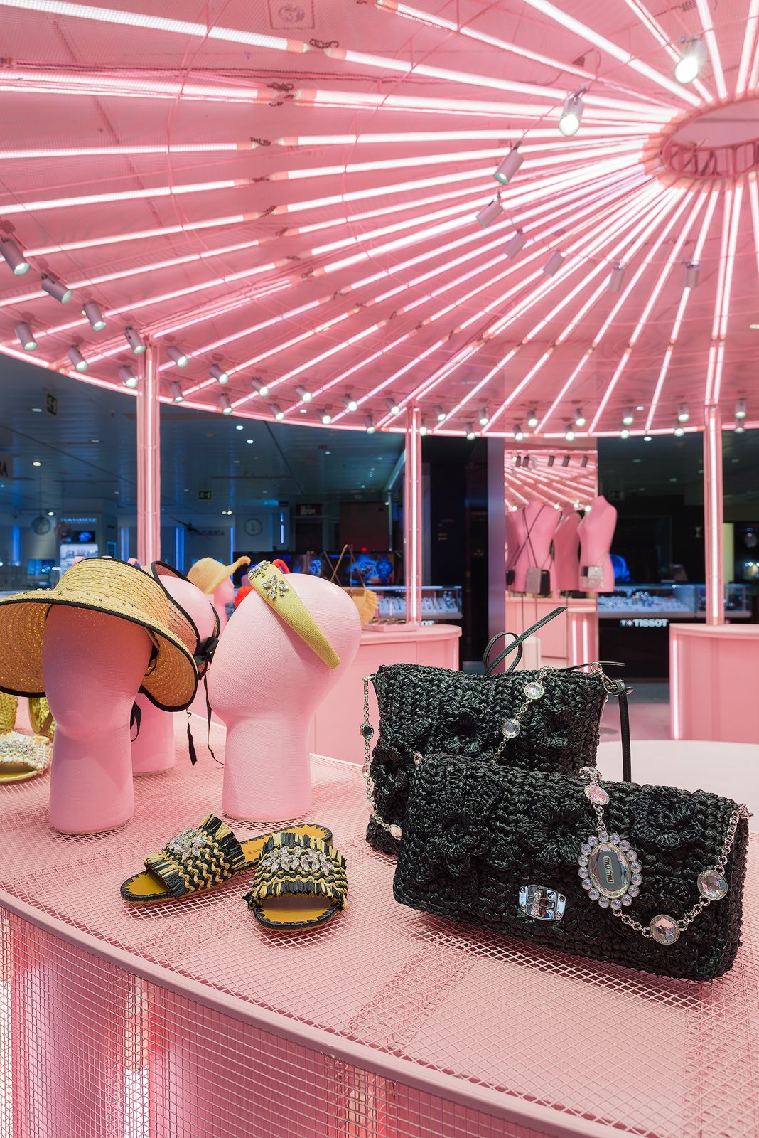 Sombreros y bolsos exhibidos en cabezas de maniquí rosas bajo vibrante iluminación rosa en la tienda pop-up de Miu Miu.