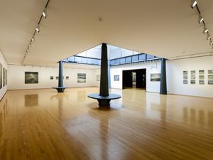 Galeria d'art amb terra de fusta polida, amb grans pintures de marines a parets blanques, centrades al voltant d'un atri amb claraboia.