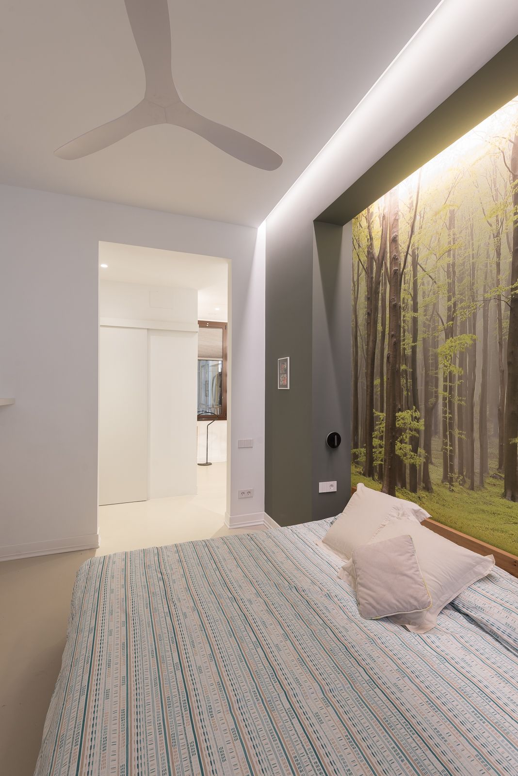Modern bedroom with forest-themed wallpaper, a ceiling fan, and soft ambient lighting.
