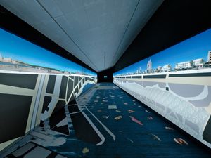 Una sala d'exposició llarga i estreta amb imatges panoràmiques d'un paisatge urbà i platja mostrades a les parets, amb plans arquitectònics detallats i mapes al terra.