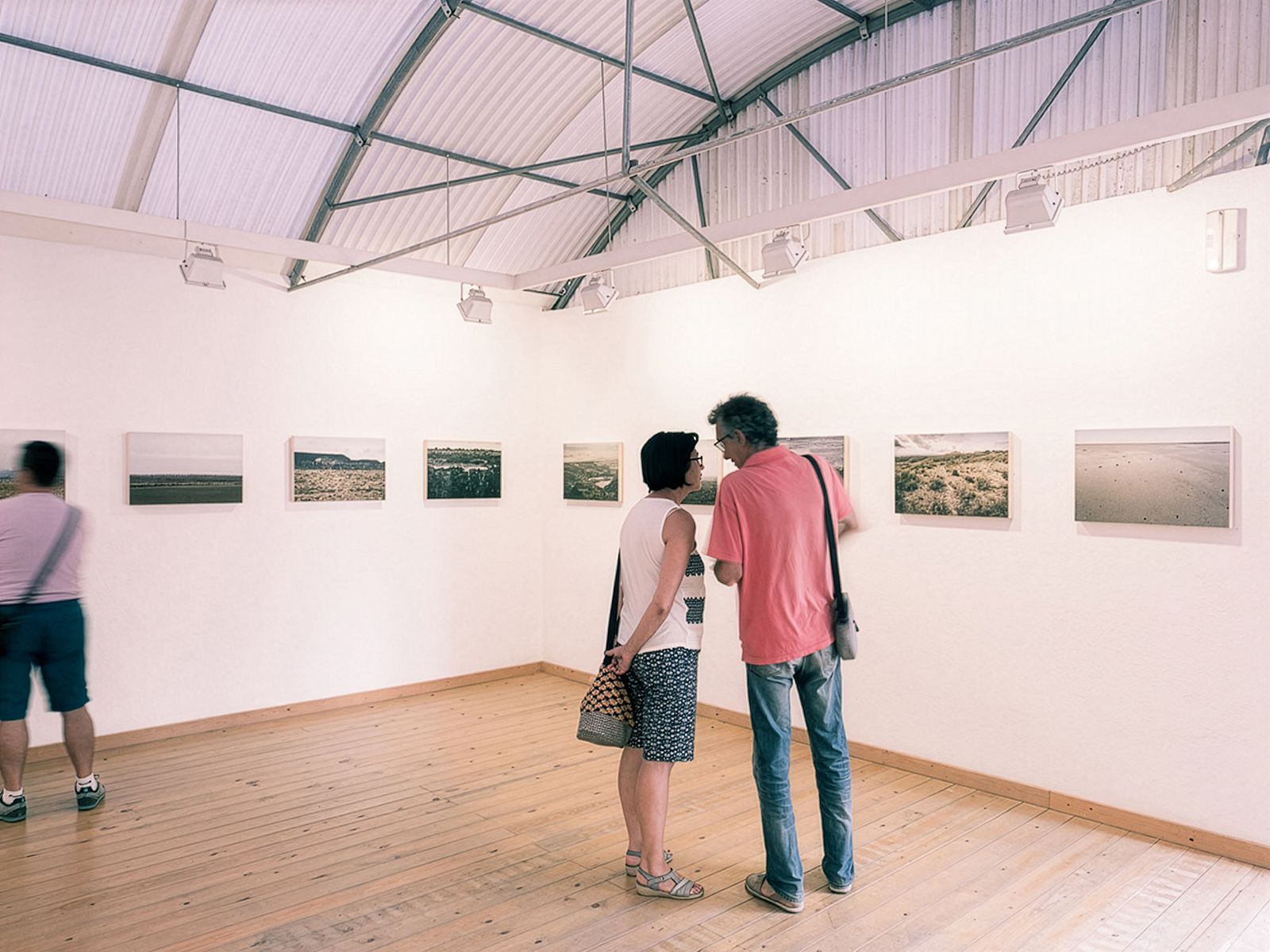 Two people talking in a gallery room with landscape photographs on the wall.