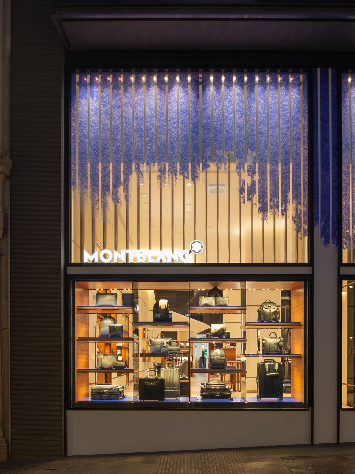 Exterior de tienda Montblanc con estantes iluminados que exhiben una variedad de bolsos y equipaje.