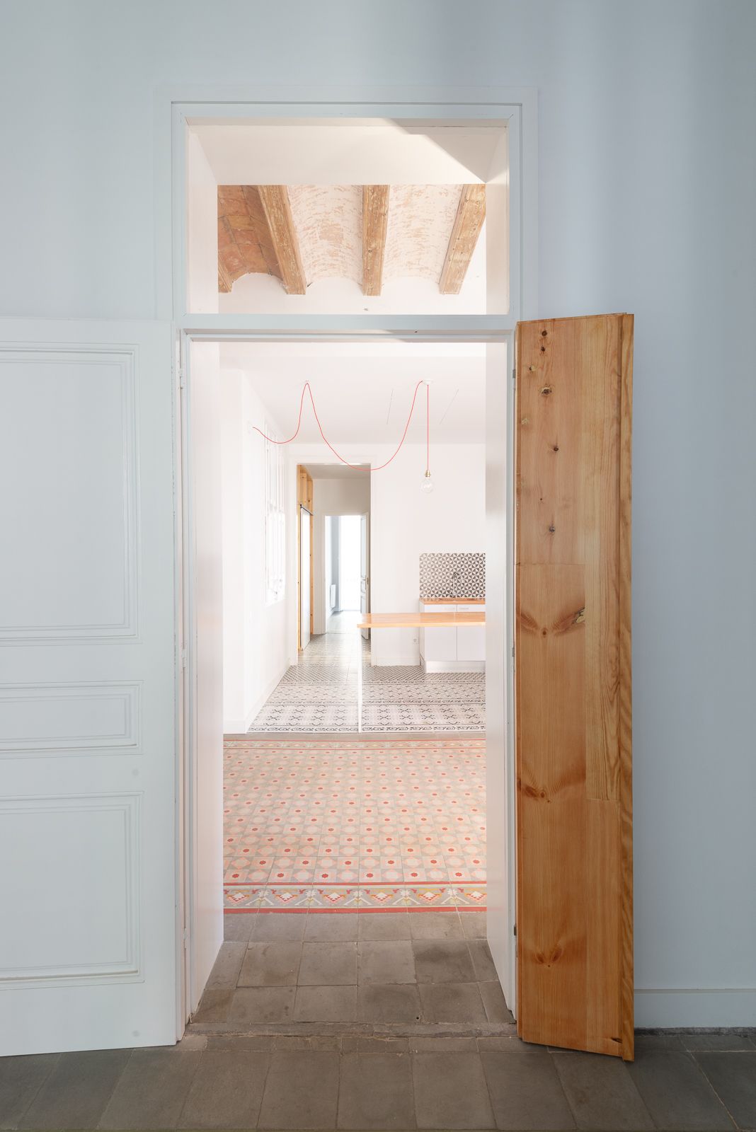 Puerta abierta que revela una habitación con baldosas de suelo estampadas y vigas de madera expuestas en el techo.