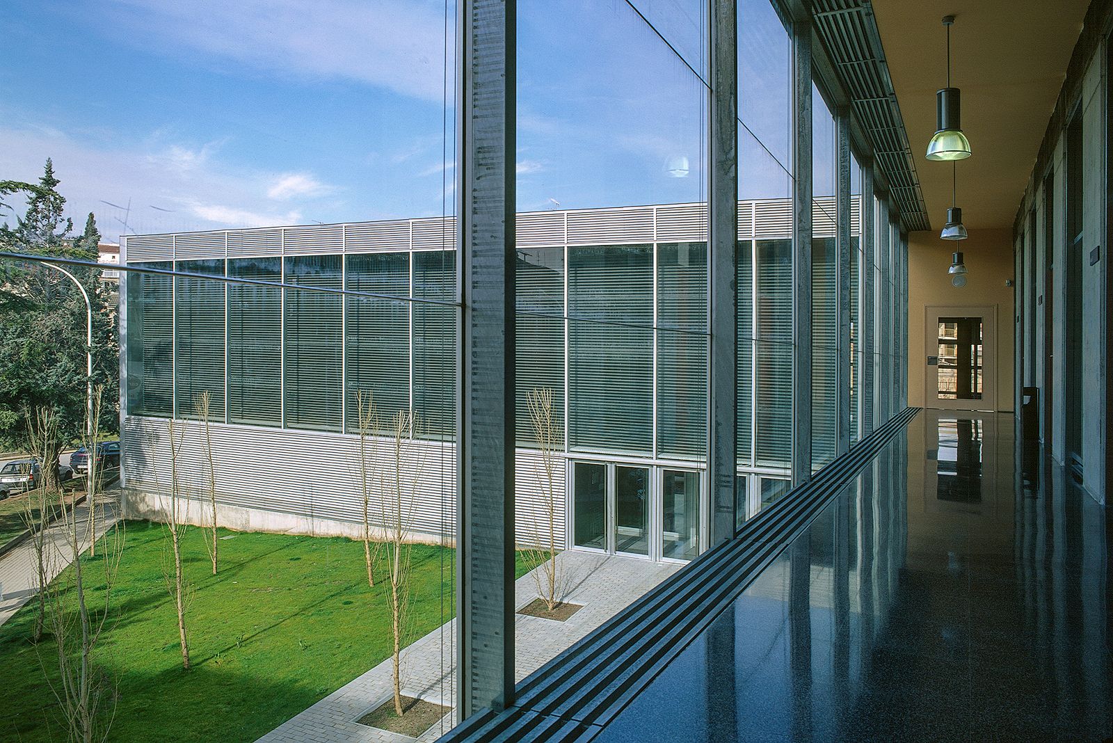 Modern building interior corridor with large windows overlooking an exterior grassy courtyard.