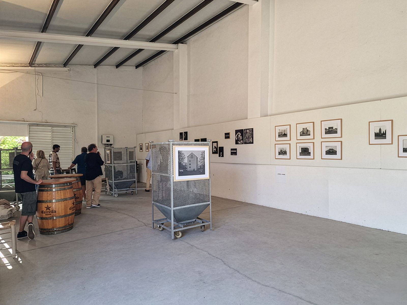 Invitados viendo fotografías en una exposición en un espacio de galería industrial abierto.