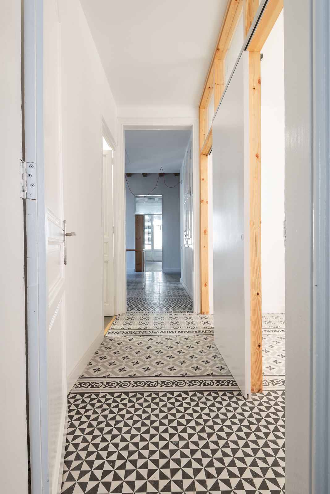 Pasillo con baldosas de suelo estampadas y un marco de madera que conduce a una habitación luminosa.