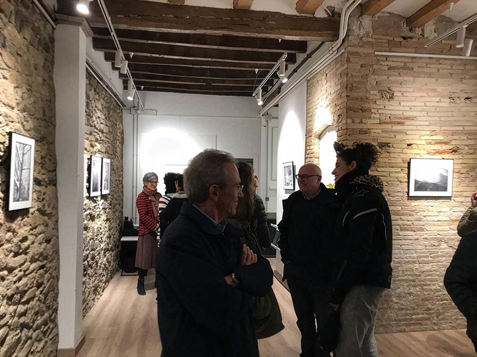 Personas viendo fotografías de paisajes en blanco y negro en paredes de piedra en una inauguración de galería de arte.