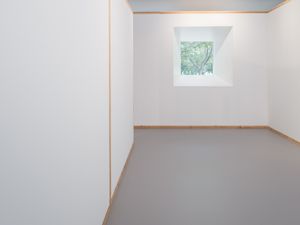 Interior minimalista amb parets blanques i marcs de fusta, amb una sola finestra que proporciona vistes als arbres exteriors.