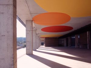 Dissenys circulars colorits al sostre projecten ombres sobre un passadís cobert amb columnes de formigó.
